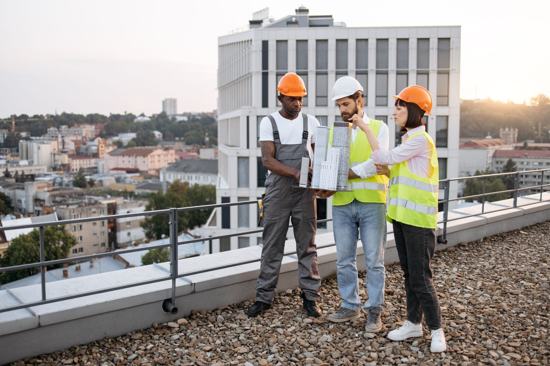 Three construction workers on a rooftop reviewing blueprints in front of a city backdrop.
