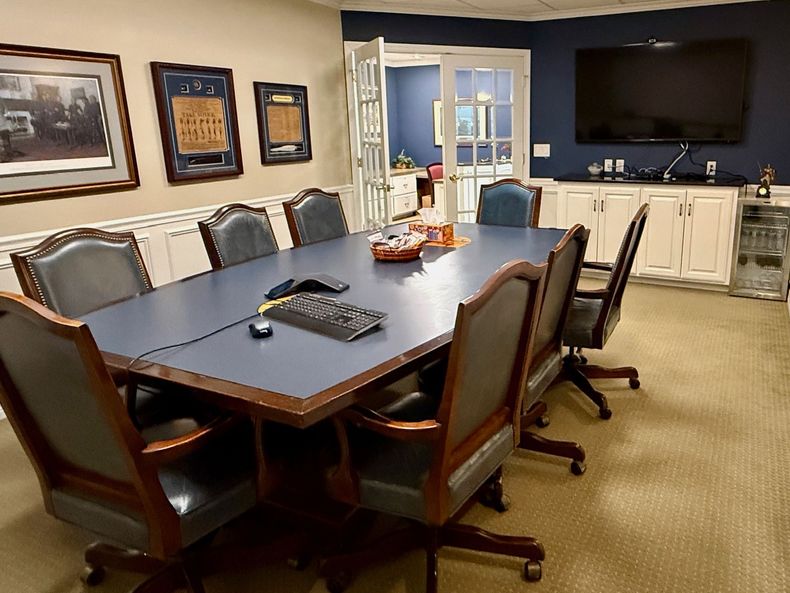 Conference room with dark wood table, black chairs, wall art, and a TV on a cabinet.