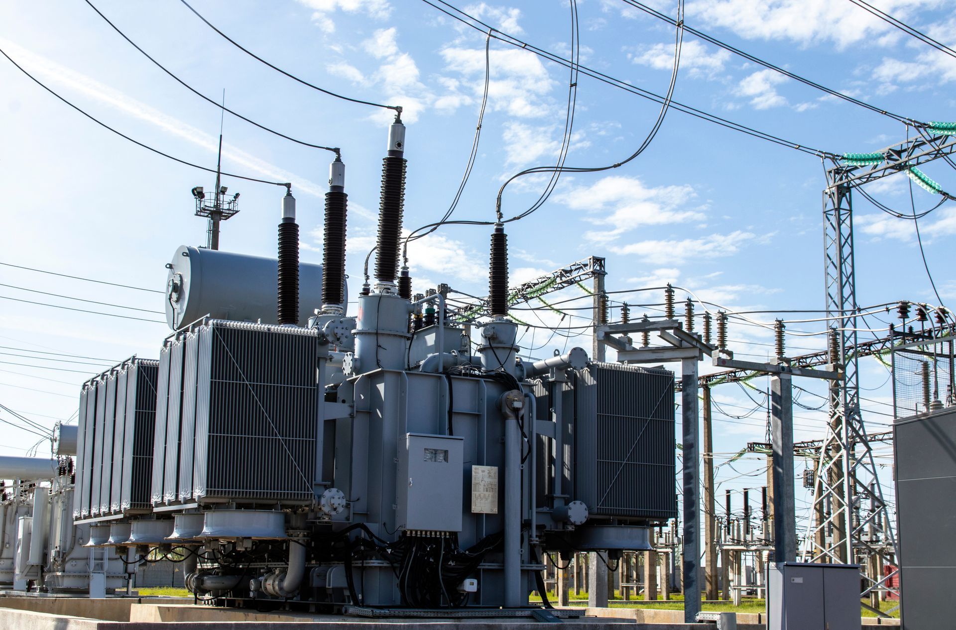 A high voltage power transformer standing tall against a clear sky, with its various components and insulators visible.