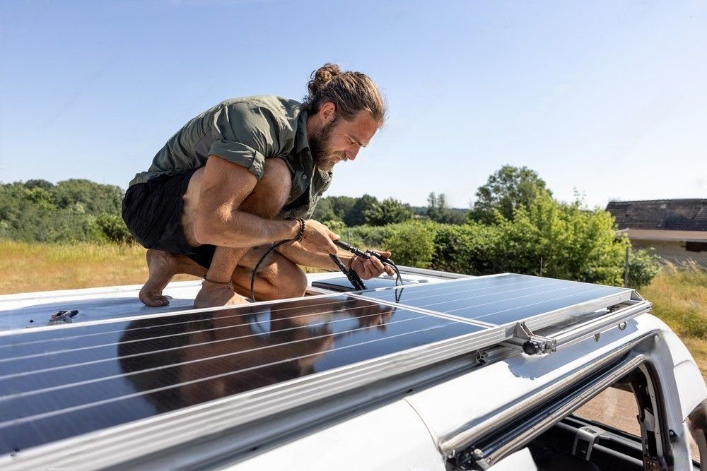 A man on top of a camper van connecting solar panels for power generation.