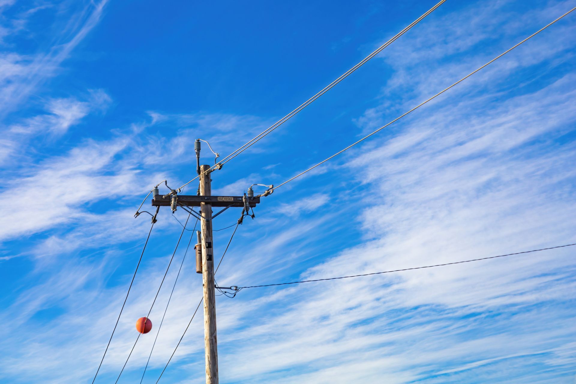 An electric utility pole with multiple lines against a clear blue sky and fluffy white clouds.