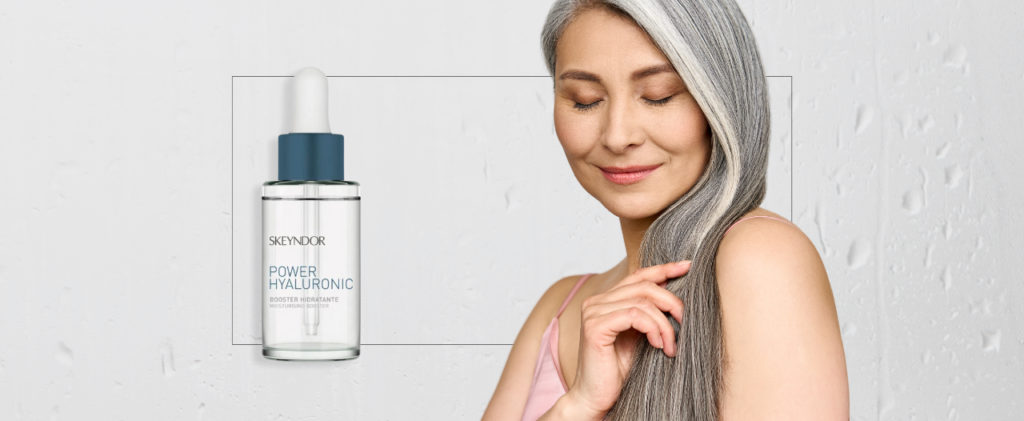 Una mujer con cabello gris sostiene su cabello frente a una botella de Booster Power Hiluronic