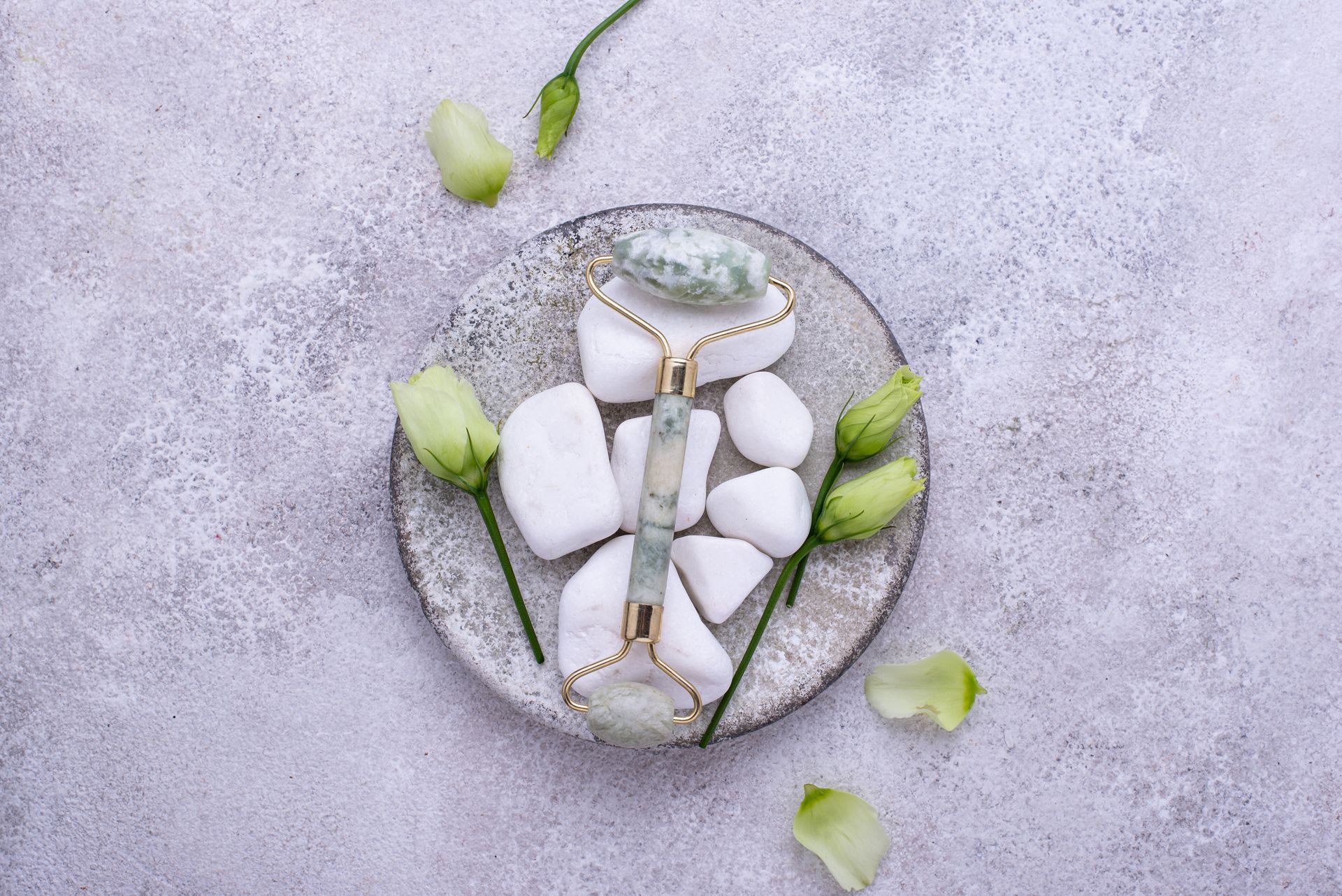 Un rodillo de jade está en un plato con rocas y flores.