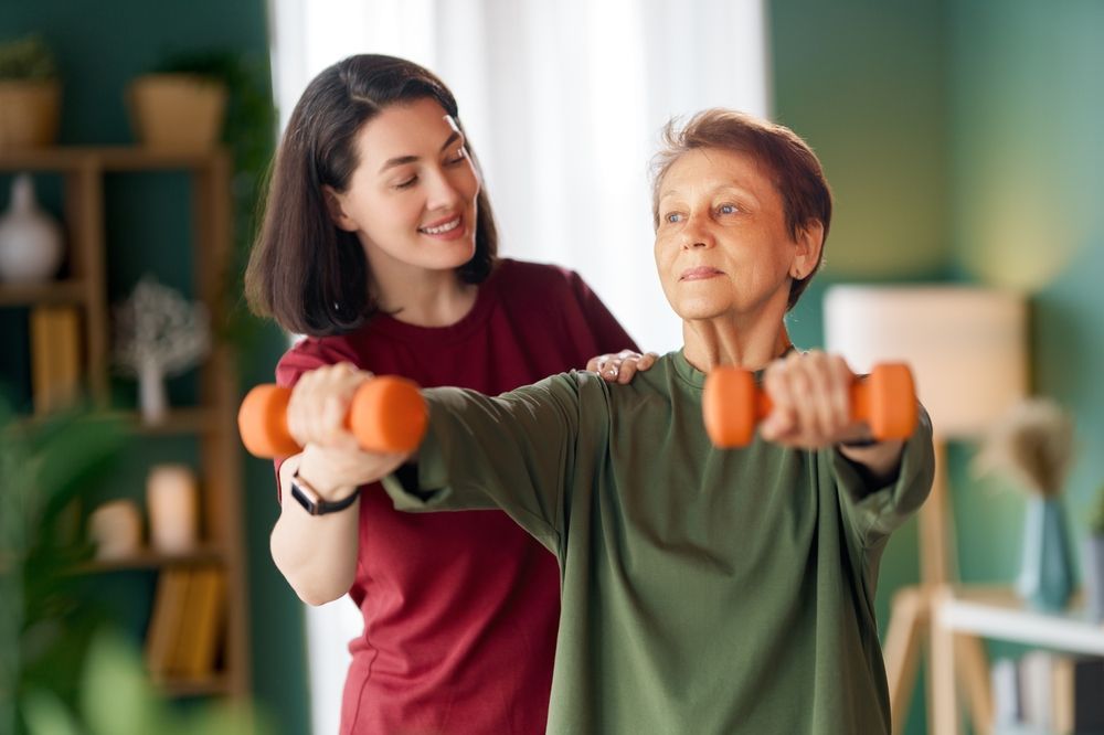 Woman helps another with arm exercises using weights indoors.