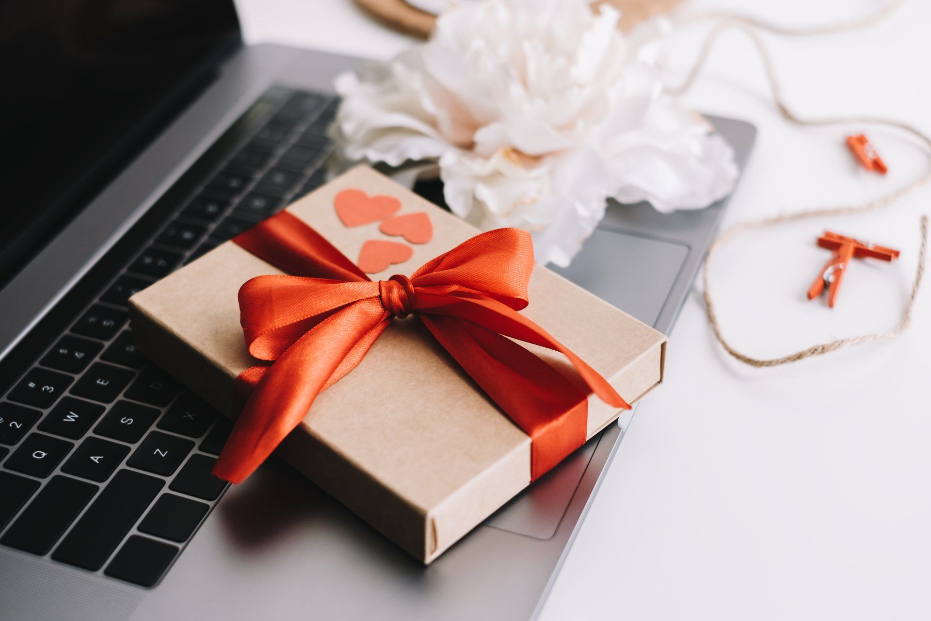 Gift box with red ribbon and hearts on the table near laptop.