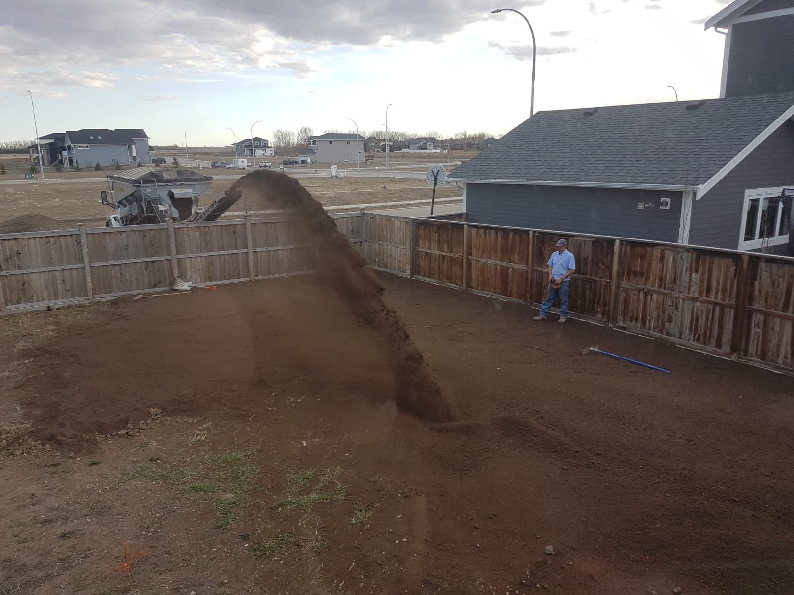 A man is standing next to a pile of dirt in front of a house.