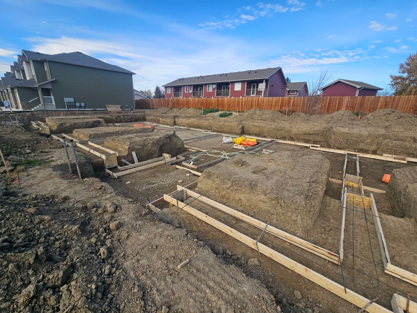 A construction site with a house in the background and a lot of dirt.