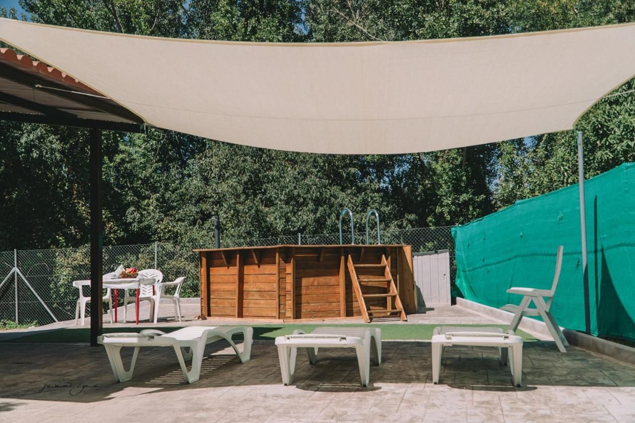 Piscina de madera con tumbonas y vela de sombra; entorno al aire libre.
