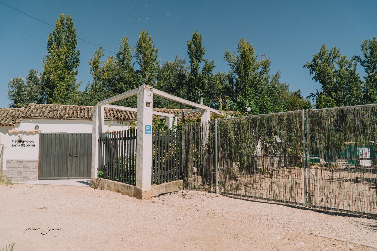 Entrada a un edificio con una puerta gris, enrejado y árboles al fondo.