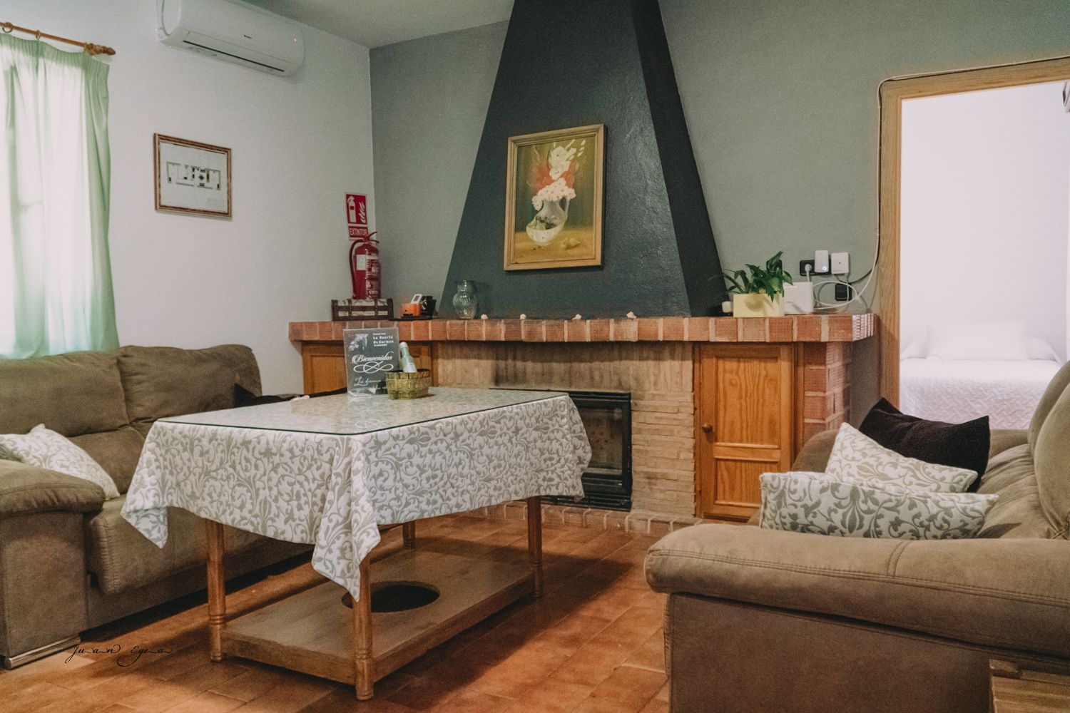 Acogedora sala de estar con chimenea, dos sofás y una mesa cubierta con un mantel estampado.