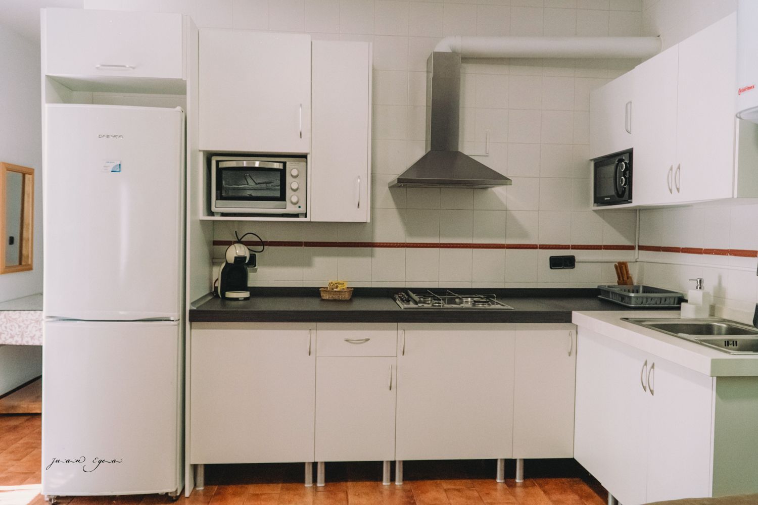 Cocina blanca con refrigerador, gabinetes, microondas, estufa y campana extractora.