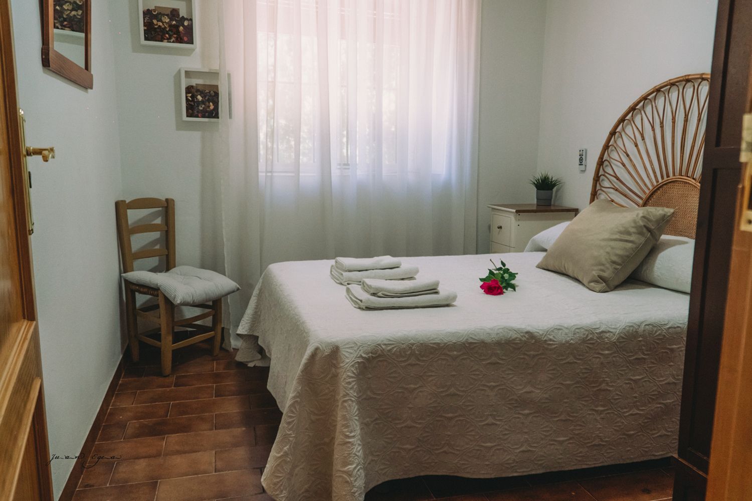 Dormitorio con cama, silla y cómoda. Color beige con cortinas blancas.