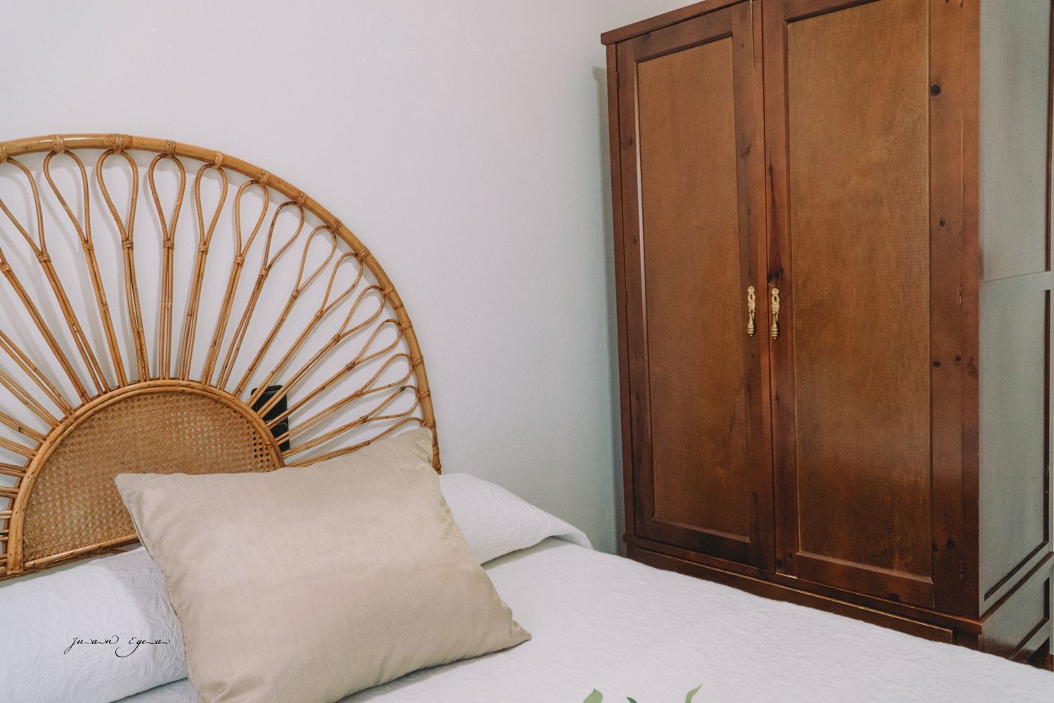 Cama con cabecera tejida, almohada color canela y armario de madera en un dormitorio.