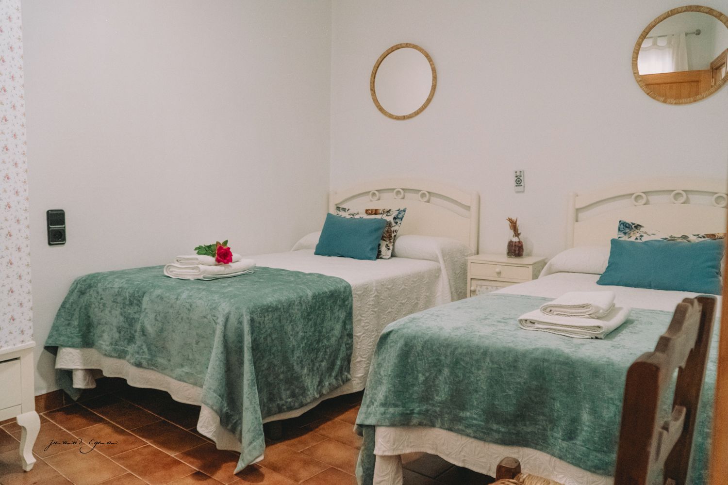 Dos camas individuales en una habitación blanca con mantas turquesas, espejos y pisos de madera.