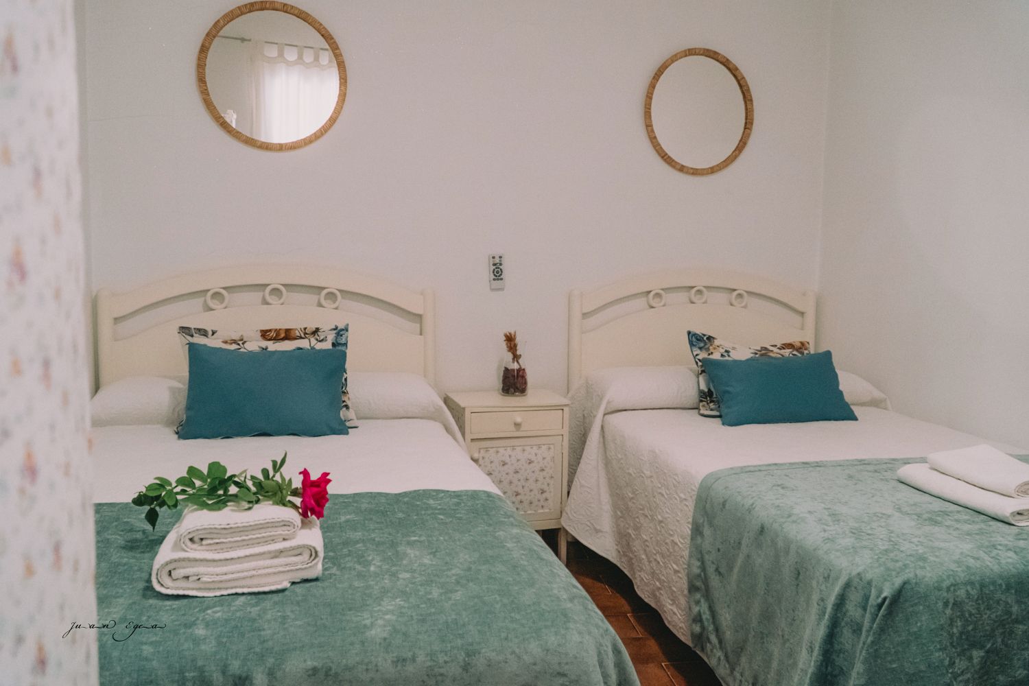 Dos camas individuales en una habitación, cada una con ropa de cama azul y blanca. Dos espejos dorados cuelgan de la pared blanca.
