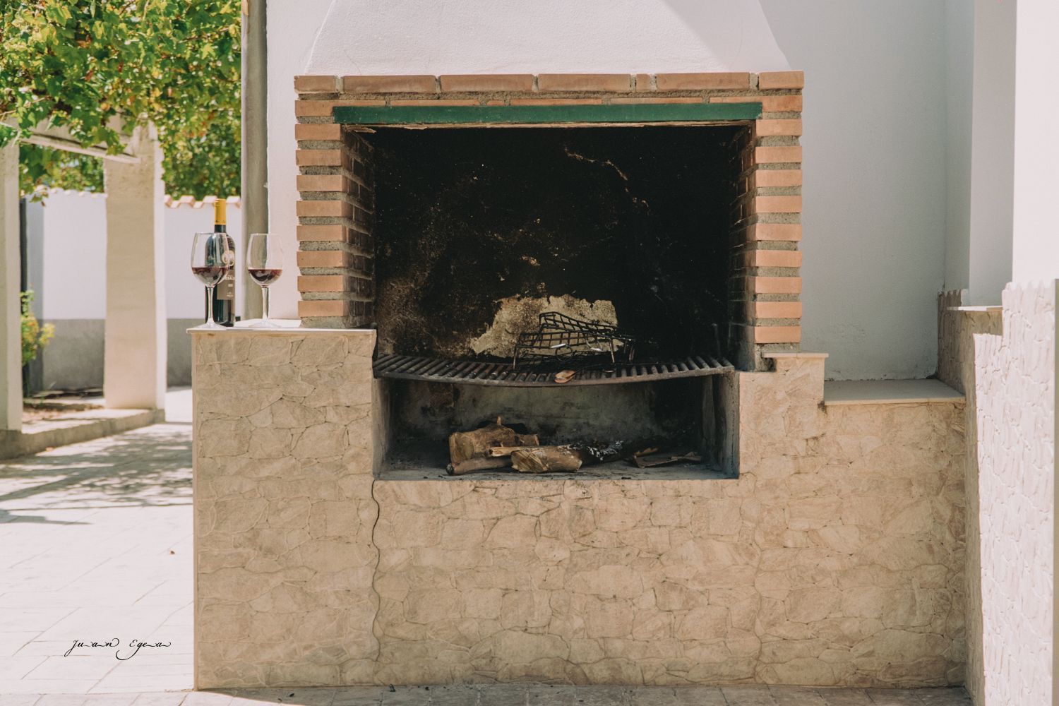 Parrilla de barbacoa de ladrillo con leña, situada contra una pared blanca, al aire libre.