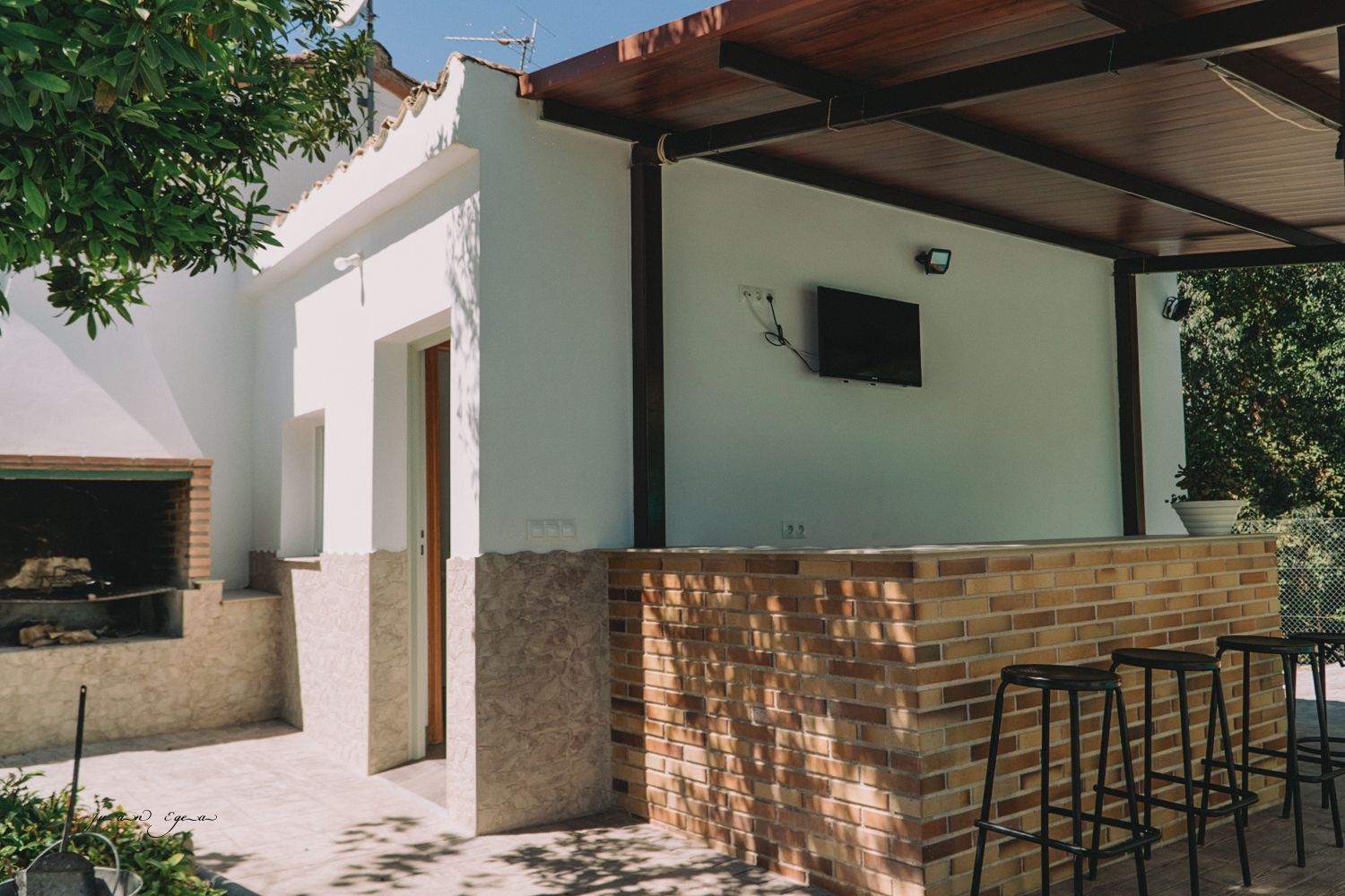Cocina al aire libre con barra de ladrillo, parrilla y asientos cubiertos.