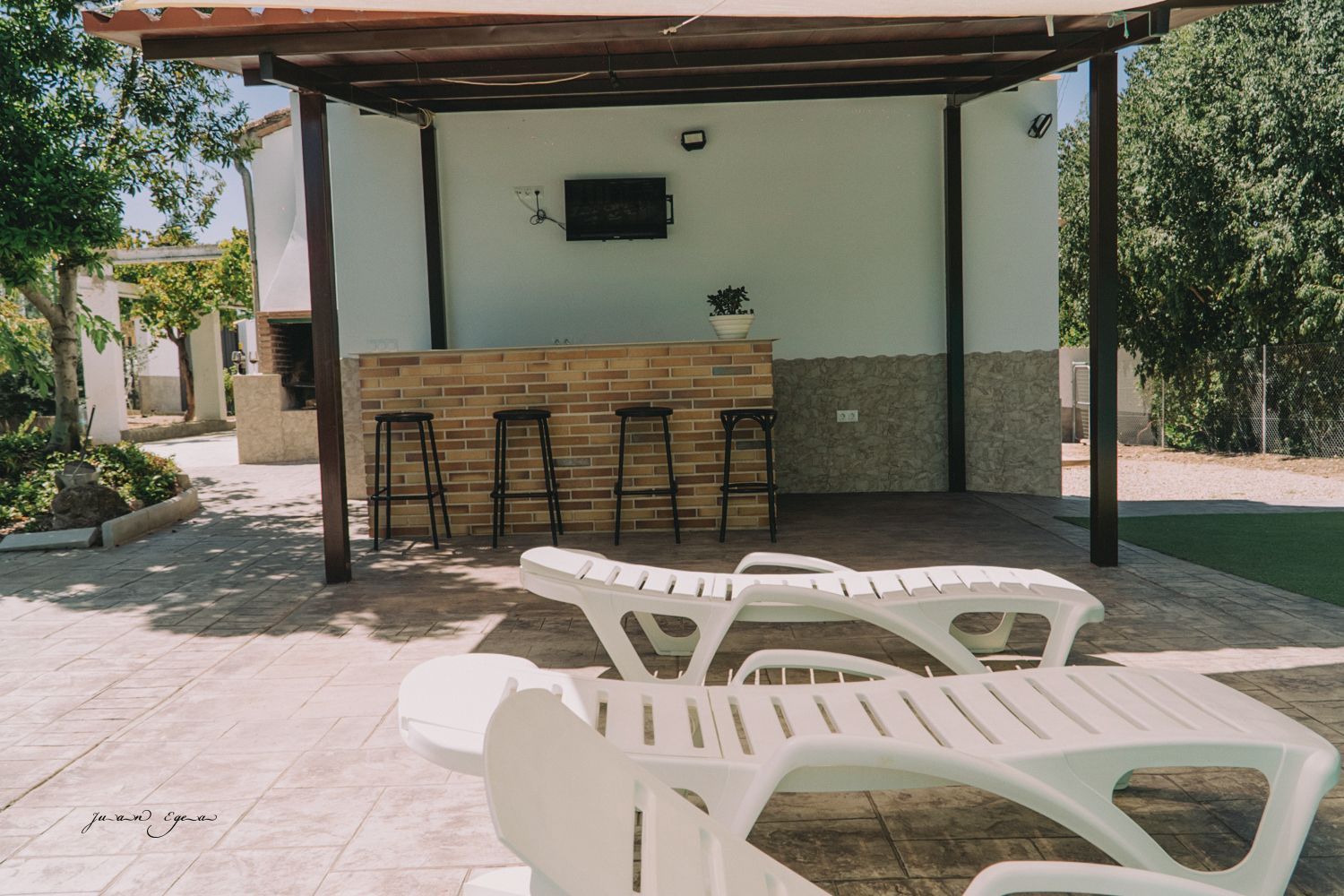 Bar al aire libre con taburetes y tumbonas bajo una pérgola.