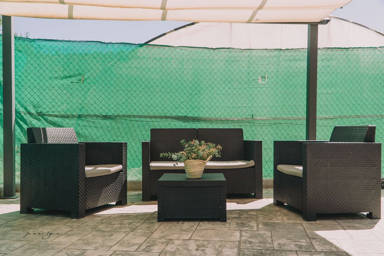 Muebles de patio ubicados en un área pavimentada con una cerca verde al fondo y un dosel blanco.