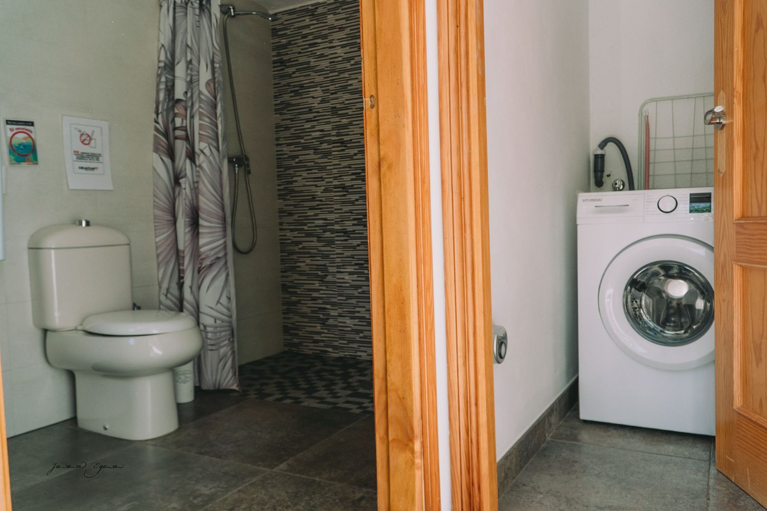 Baño con inodoro, ducha y lavadora, visible a través de una puerta abierta.