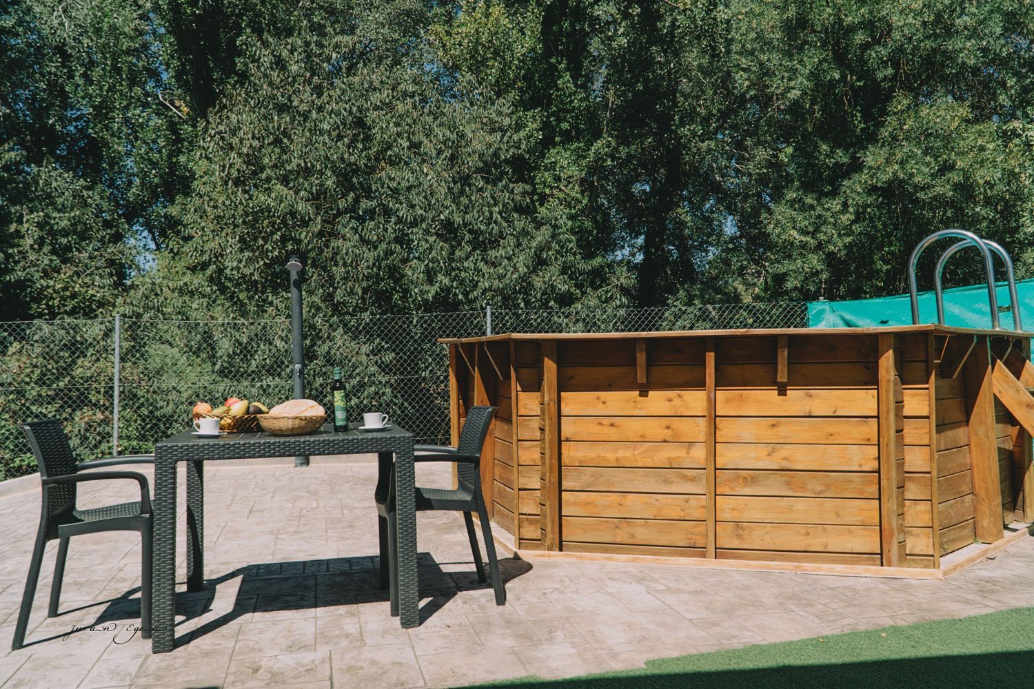 Piscina de madera con mesa y sillas en un patio trasero, rodeada de árboles.