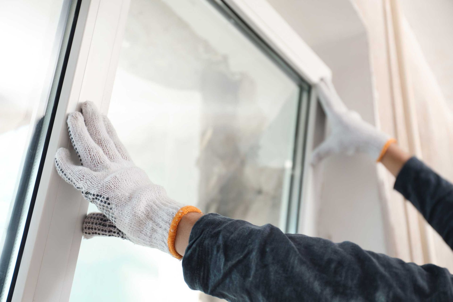 Hands in gloves align a new window frame during home window replacement installation.