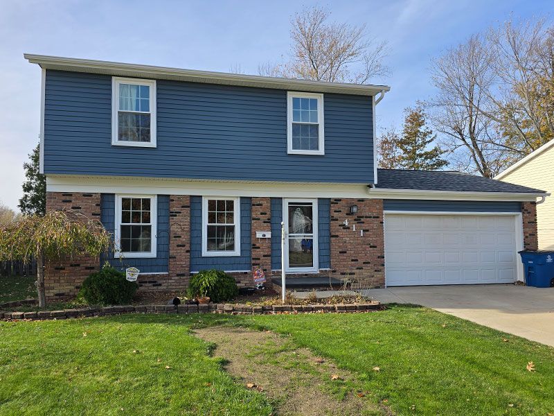 Two-story house with blue horizontal siding, brick accents, white trim, a front door, and an attached two-car garage.