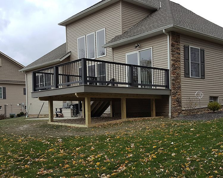 A tan, two-story suburban house featuring an elevated wooden deck with black railings in the backyard.