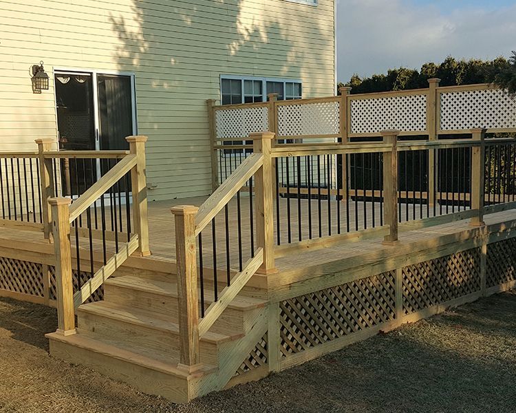 A wooden backyard deck with black metal balusters, matching stairs, and a white lattice privacy screen against a house.