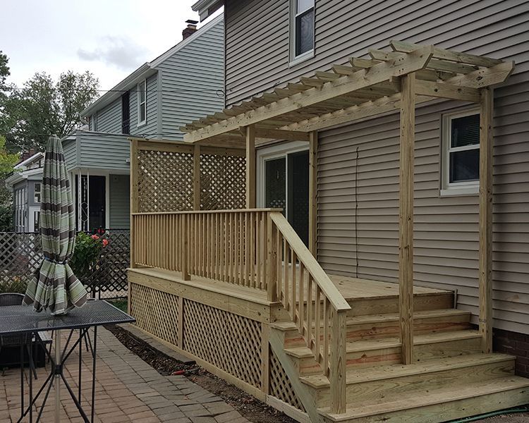 A new, light-colored wooden deck with lattice skirting, stairs, and a pergola attached to the back of a beige-sided house.