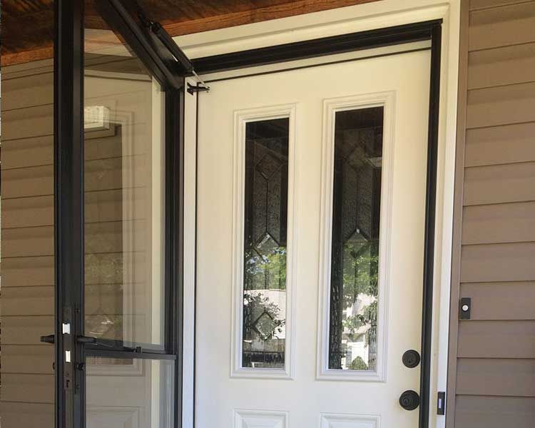 A white door with two vertical glass panels next to a partially open black storm door on a house with brown siding.