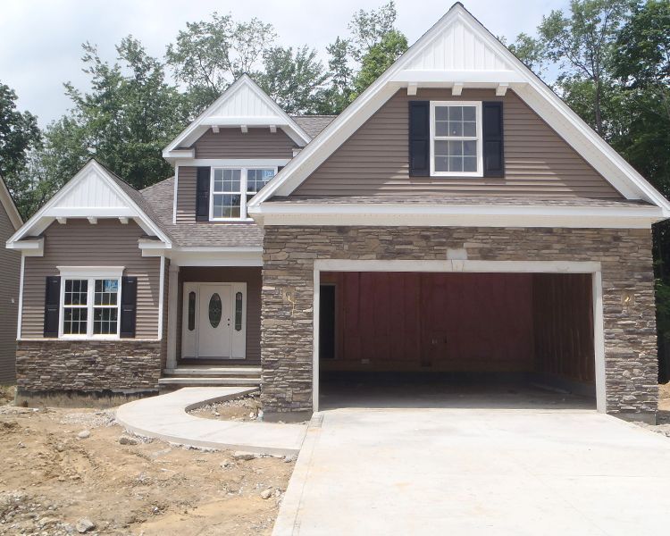 A two-story suburban house with a stone and brown siding exterior, featuring an attached garage and a front walkway.