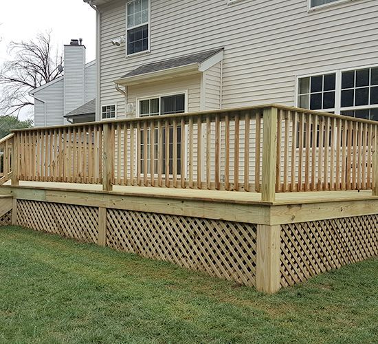 A newly built light-colored wooden deck with lattice skirting, attached to the back of a beige siding house.