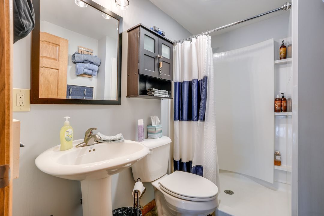 Small bathroom with white sink, toilet, and shower. Blue and white towels and shower curtain. Dark brown cabinet.