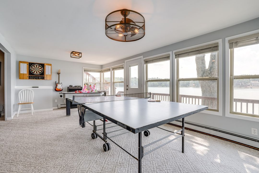 Recreation room with ping pong table, windows overlooking lake. Dartboard, guitar, ceiling fans. Carpeted floor.