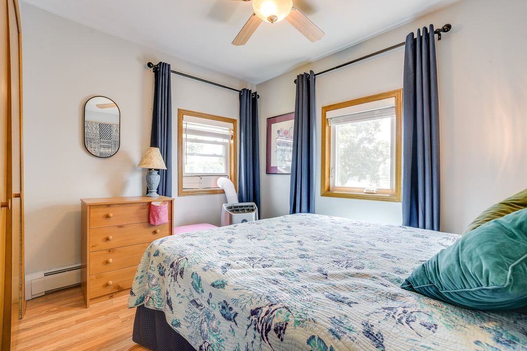 Bedroom with bed, dresser, windows, blue curtains, and wood floors.
