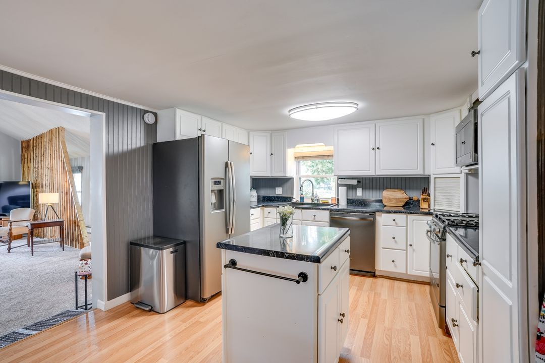 Kitchen with white cabinets, stainless steel appliances, and island. Light wooden floor.