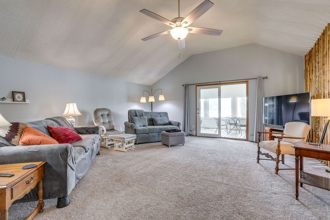 Spacious living room with gray carpet, sofas, chairs, TV, and sliding door to patio.