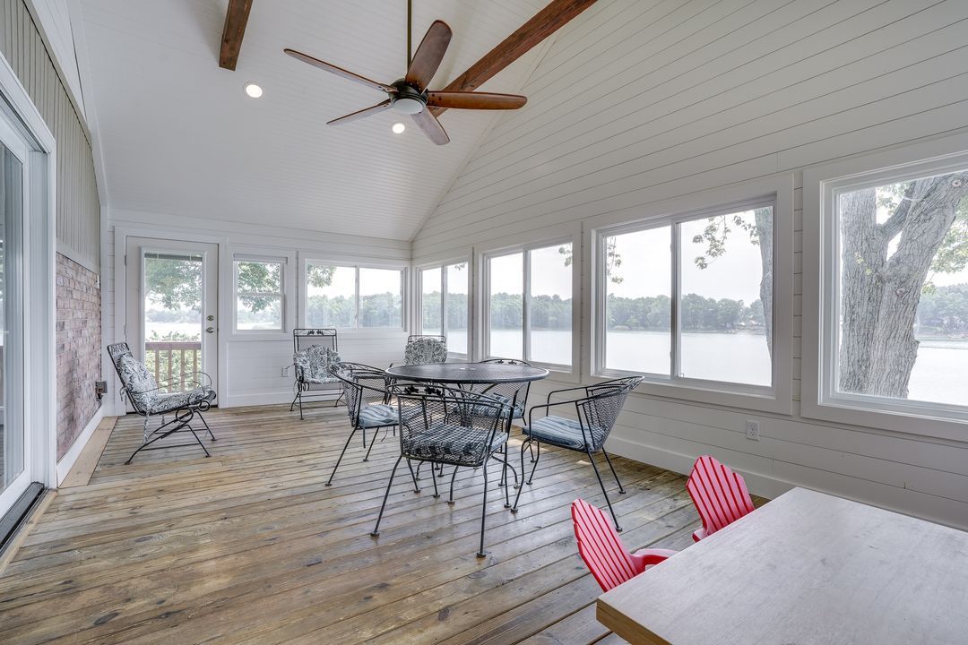Sunroom with lake view, wood floor, tables, chairs, and large windows.