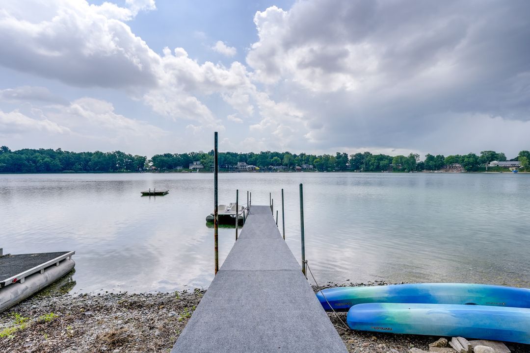 Dock extends into lake with kayaks, trees and cloudy sky.