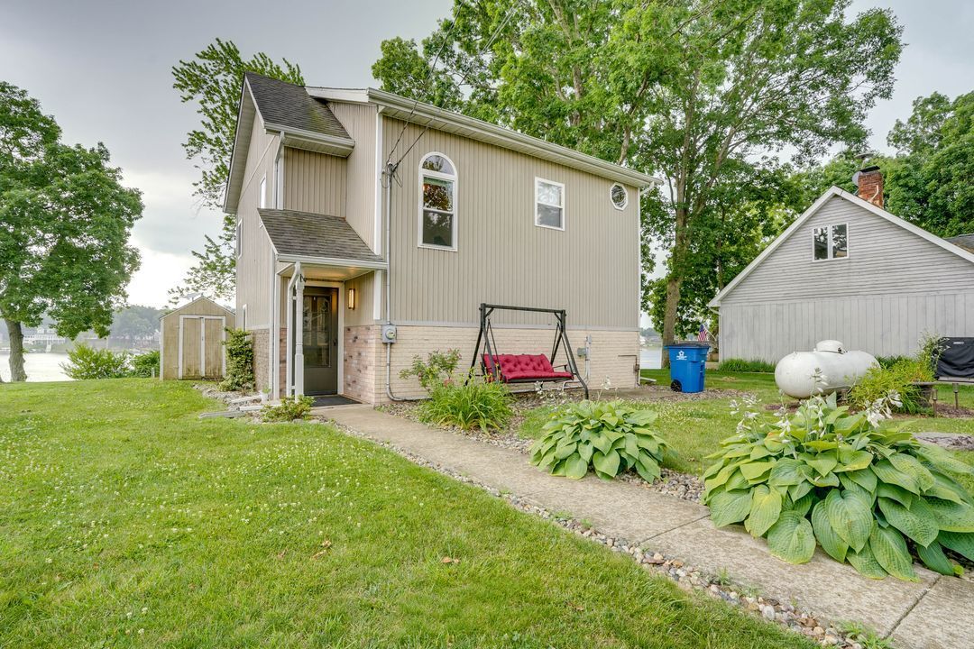 A light-colored house with a swing, path, and a lake view, on a grassy lot.