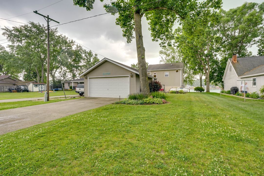 A beige house with a garage, driveway, and large grassy lawn under a cloudy sky.