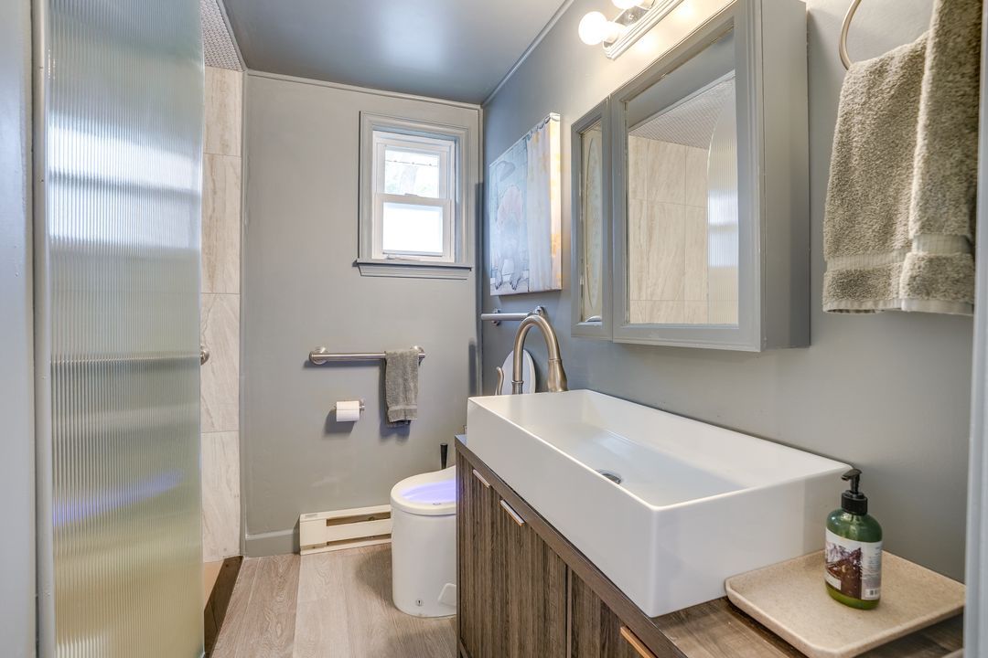Gray bathroom with modern sink, cabinet, and shower. Small window.