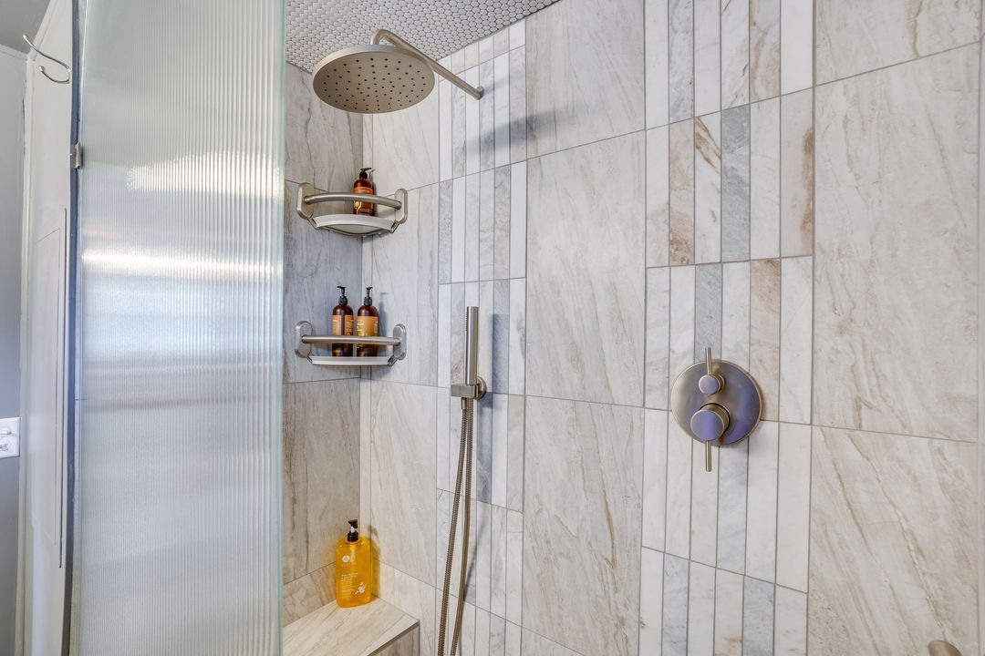 Shower with stone tile walls, large rain shower head, handheld shower, and glass door.