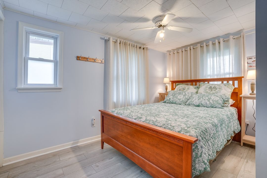 Bedroom with a wooden bed, floral bedding, window with curtains, and a ceiling fan.