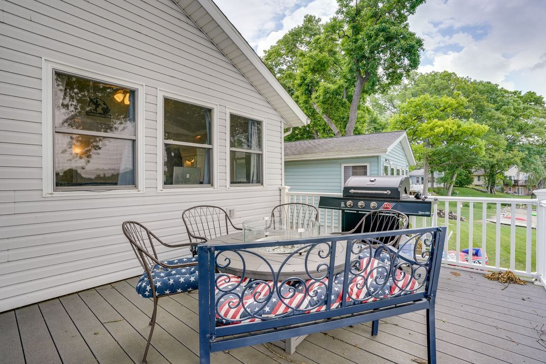 Deck of a white house with outdoor furniture, grill, and view of a lake.
