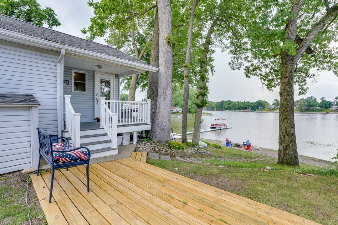 Small cottage with deck overlooking a lake, trees, and boats.