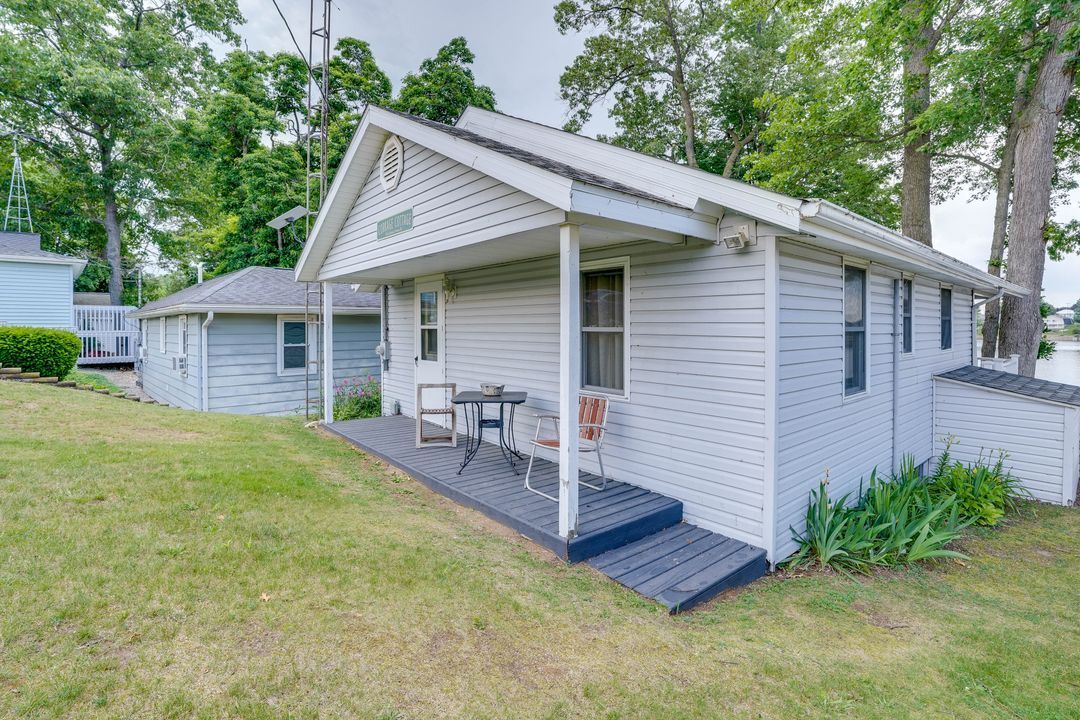 White cottage with dark gray porch, grassy yard, trees in background.