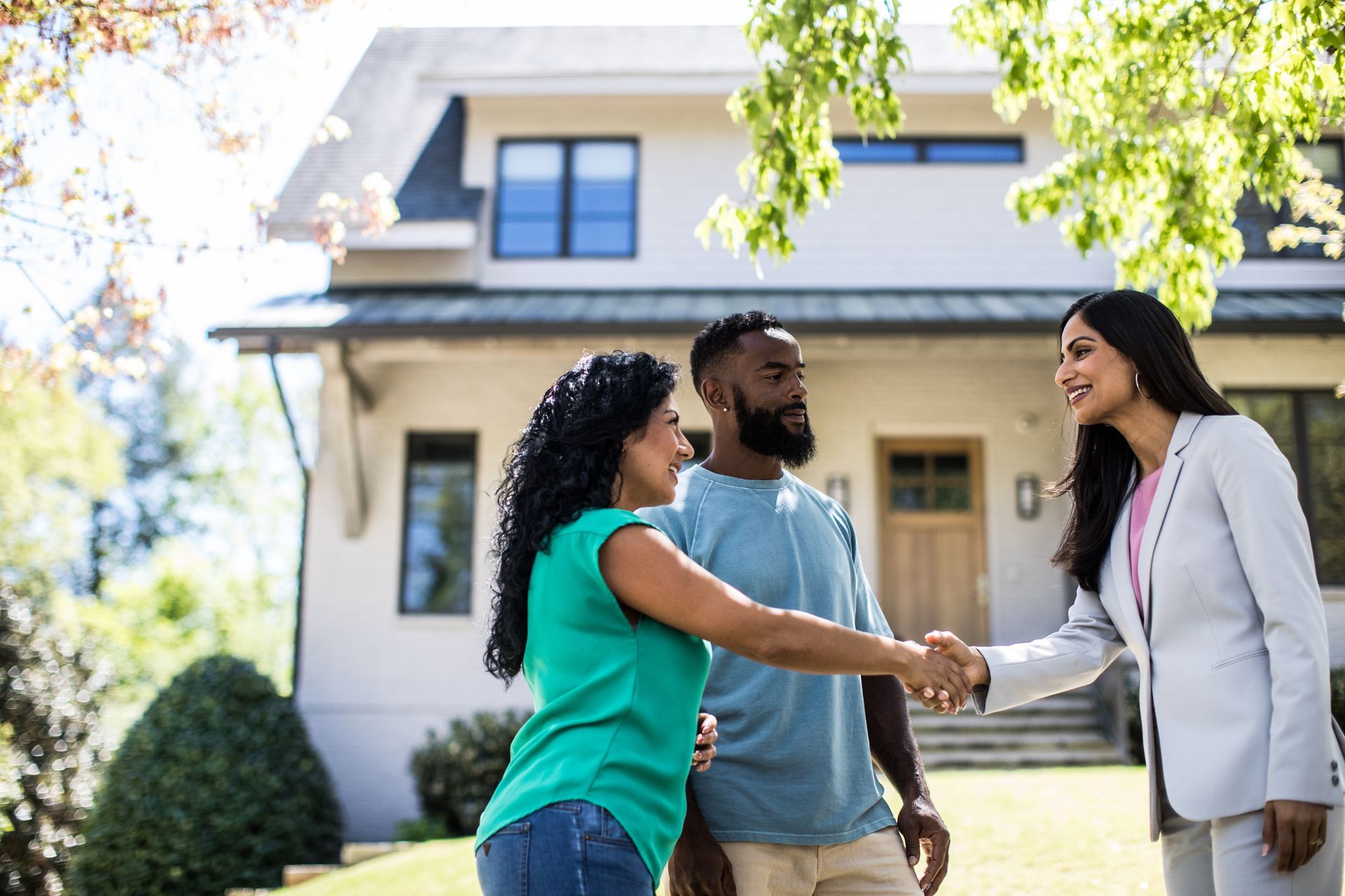 A woman is shaking hands with a man and woman in front of a house.