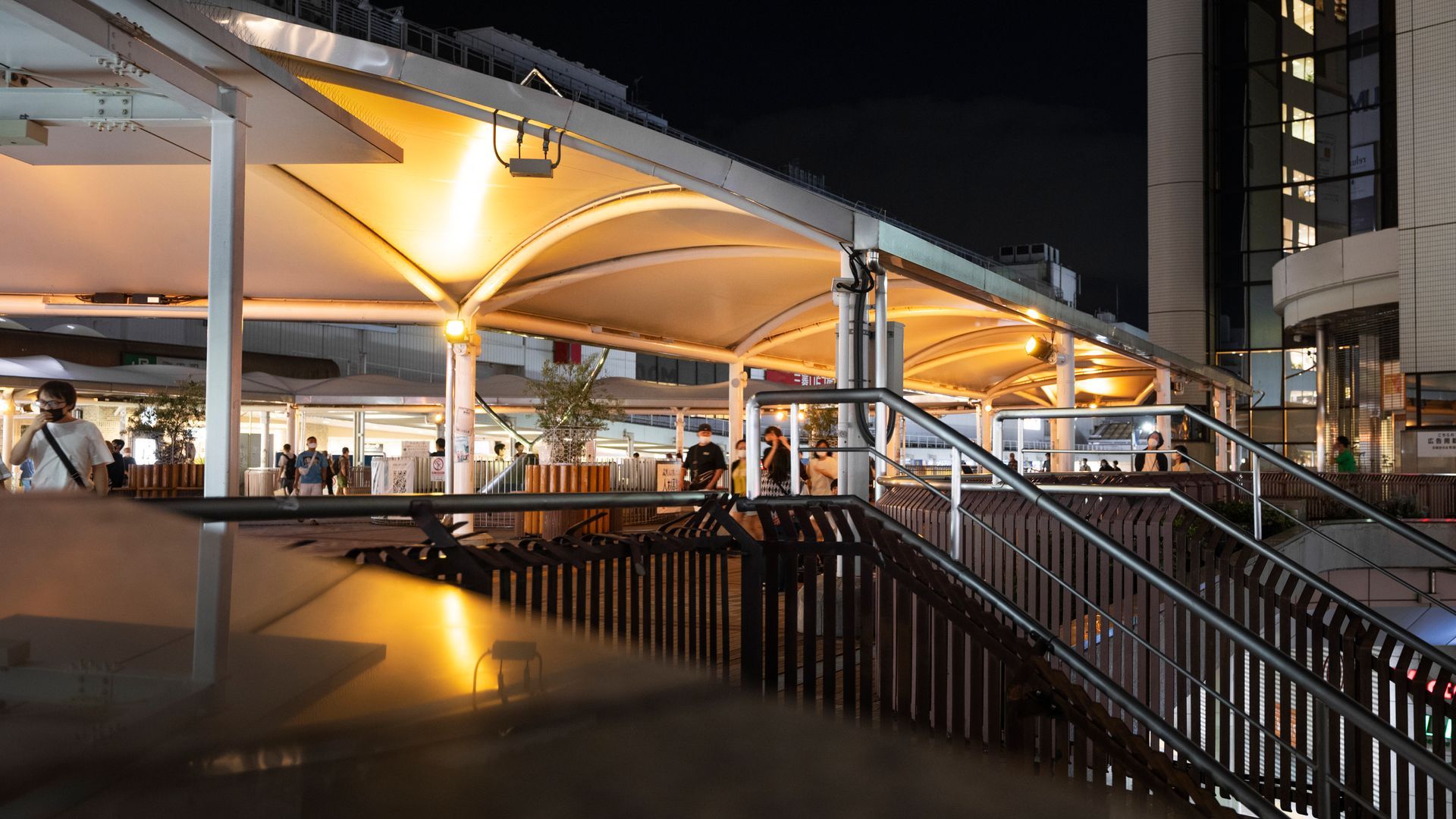 Covered outdoor walkway at night with stairs, illuminated by warm lights; people visible.